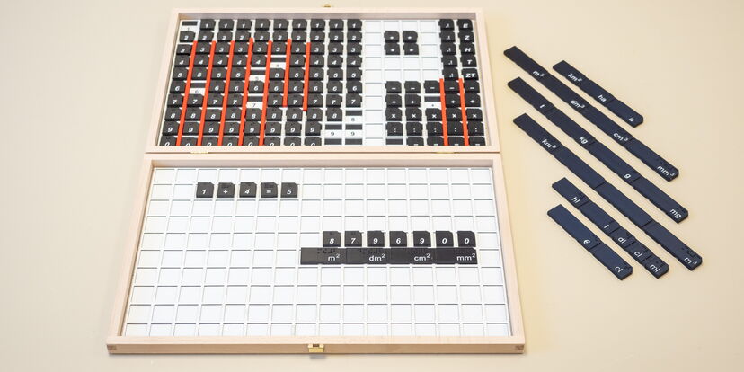 Magnetischer Rechenkasten zur Darstellung der Grundrechenarten. Auf weißem Grund liegen schwarze Ziffern- und Einheitenblättchen.