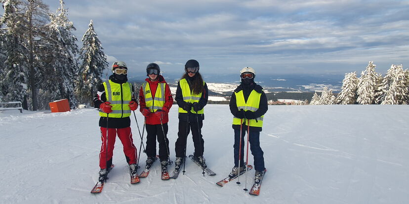 Vier Personen mit Skiern und Warnwesten auf einem Berg.