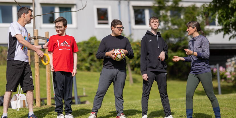 Eine Motologin macht mit 4 Teilnehmern eine Sportübung im Freien.