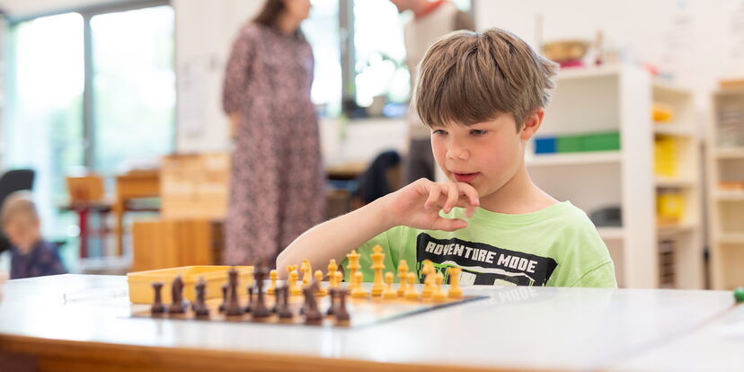 In einem Klassenraum sitzt ein Schüler konzentriert an einem Schachbrett.