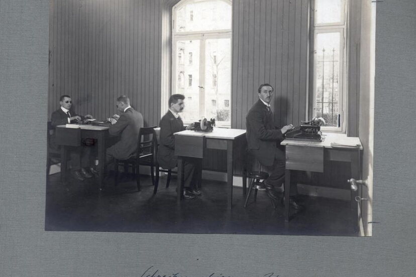 Historische Schwarzweißfotografie: Vier Männer sitzen an Punktschriftmaschinen.