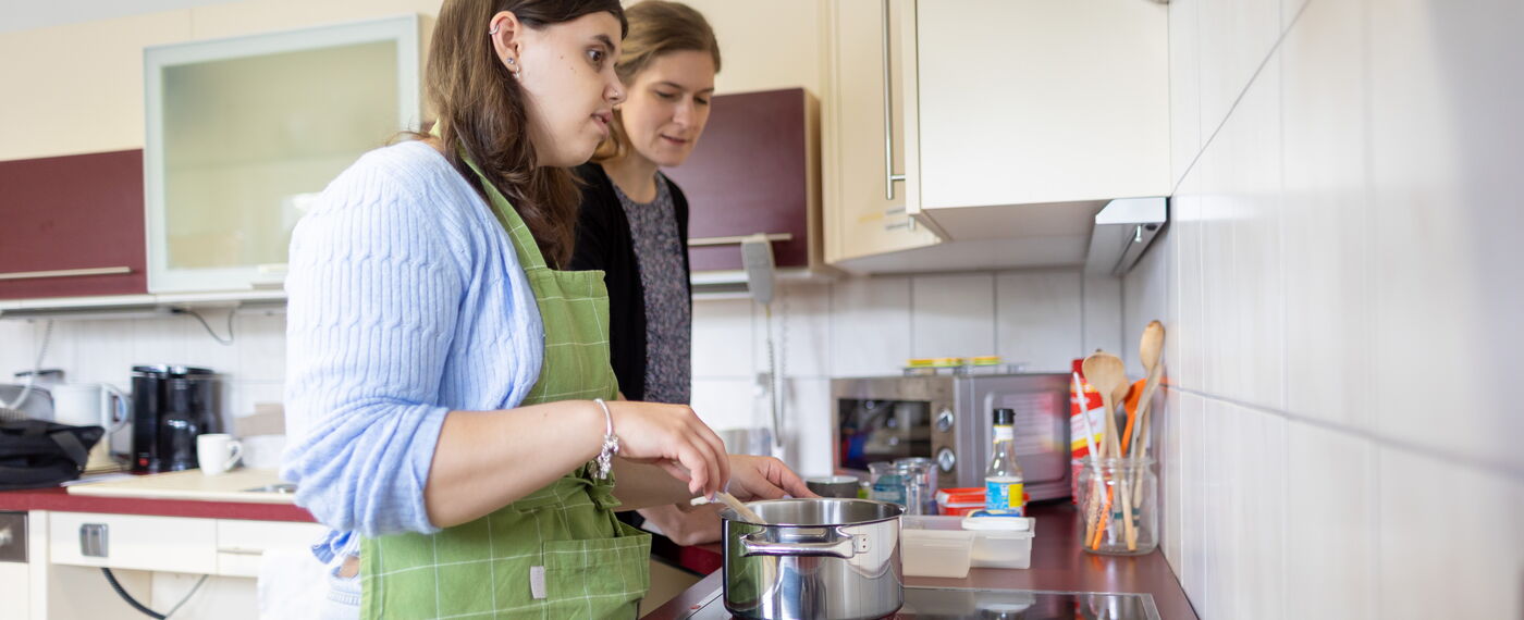 Eine Teilnehmerin und eine Lehrkraft stehen an einem Herd und kochen.