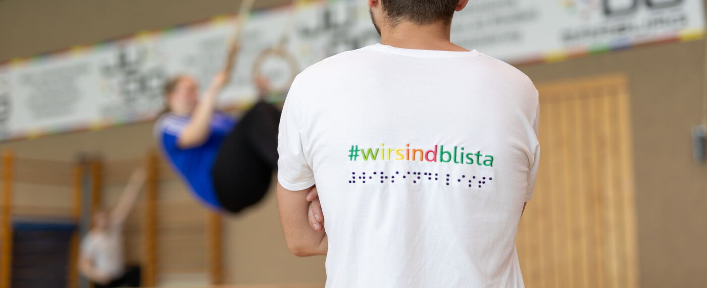 Rückansicht einer Person, die eine Schülerin beim Ringeturnen beobachtet.