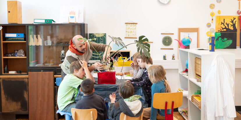 Ein Lernbegleiter demonstriert einer Gruppe Schüler*innen etwas an einer Pflanze
