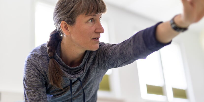 Die Motologin führt eine Gymnastikübung vor, bei der sie den Arm im Vierfüßlerstand ausstreckt.