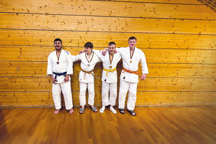 Vier junge Männer stehen mit weißen Judoanzügen in einer Sporthalle, sie tragen Medaillen um den Hals