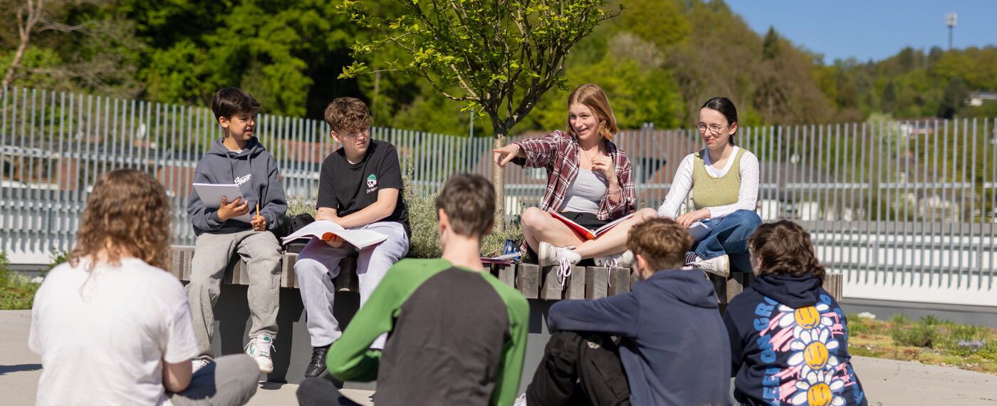 Acht Schüler*innen mit Heften auf dem Schoß sind auf der Dachterrasse in ein Gespräch vertieft.