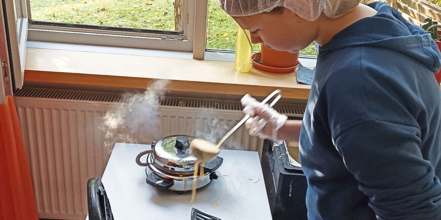 Eine Schülerin füllt Teig mit einer Schöpfkelle in ein Waffeleisen.
