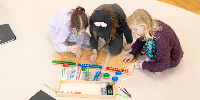 Drei Kinder arbeiten an Montessori-Materialien aus Holz