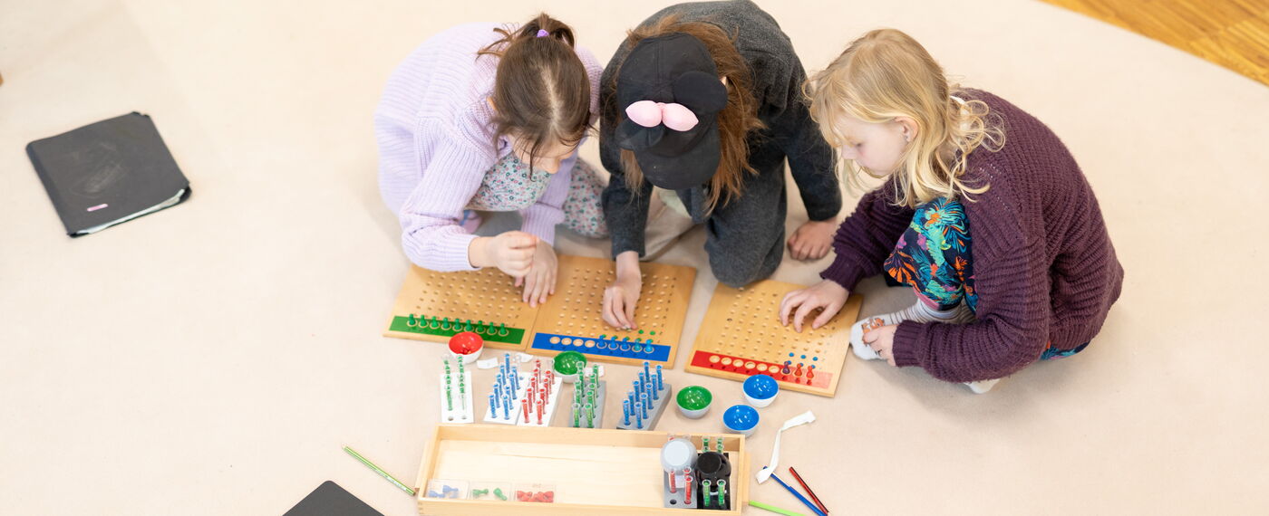 Drei Kinder arbeiten an Montessori-Materialien aus Holz