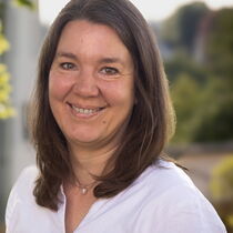 Portraitfoto Julia Schneider lächelt freundlich in die Kamera. Sie hat mittellange braune Haare und trägt eine weiße Bluse.