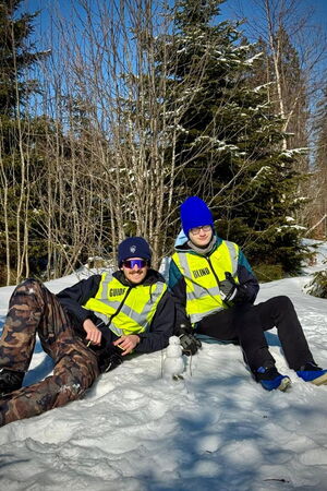 Ein Guide und ein Schüler sitzen gemeinsam bei Sonnenschein im Schnee, vor ihnen ein Miniaturschneemann.