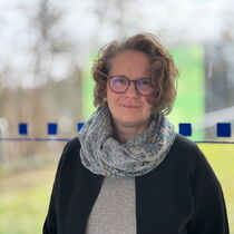 Portraitfoto Stefanie Ganz - sie hat kinnlanges gelocktes Haar und trägt ein dunkles Oberteil und einen Schal.