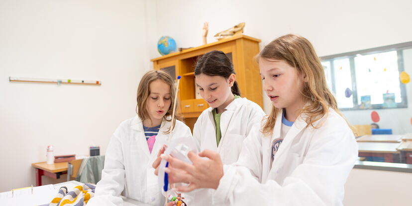 Drei Schüler*innen tragen Laborkittel und forschen gemeinsam.