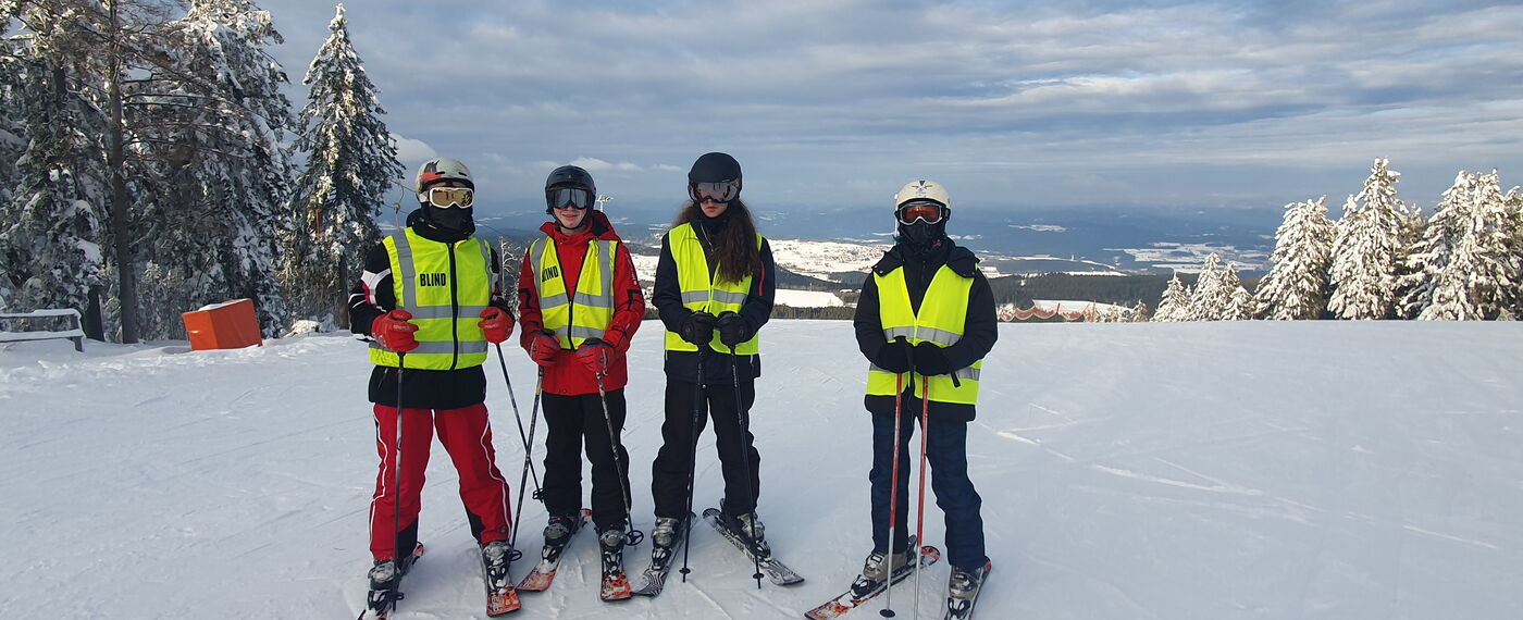 Vier Personen mit Skiern und Warnwesten auf einem Berg.