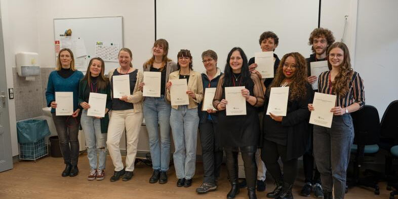 Zehn Absolventinnen und ein Absolvent zeigen stolz ihre Zeugnisse.