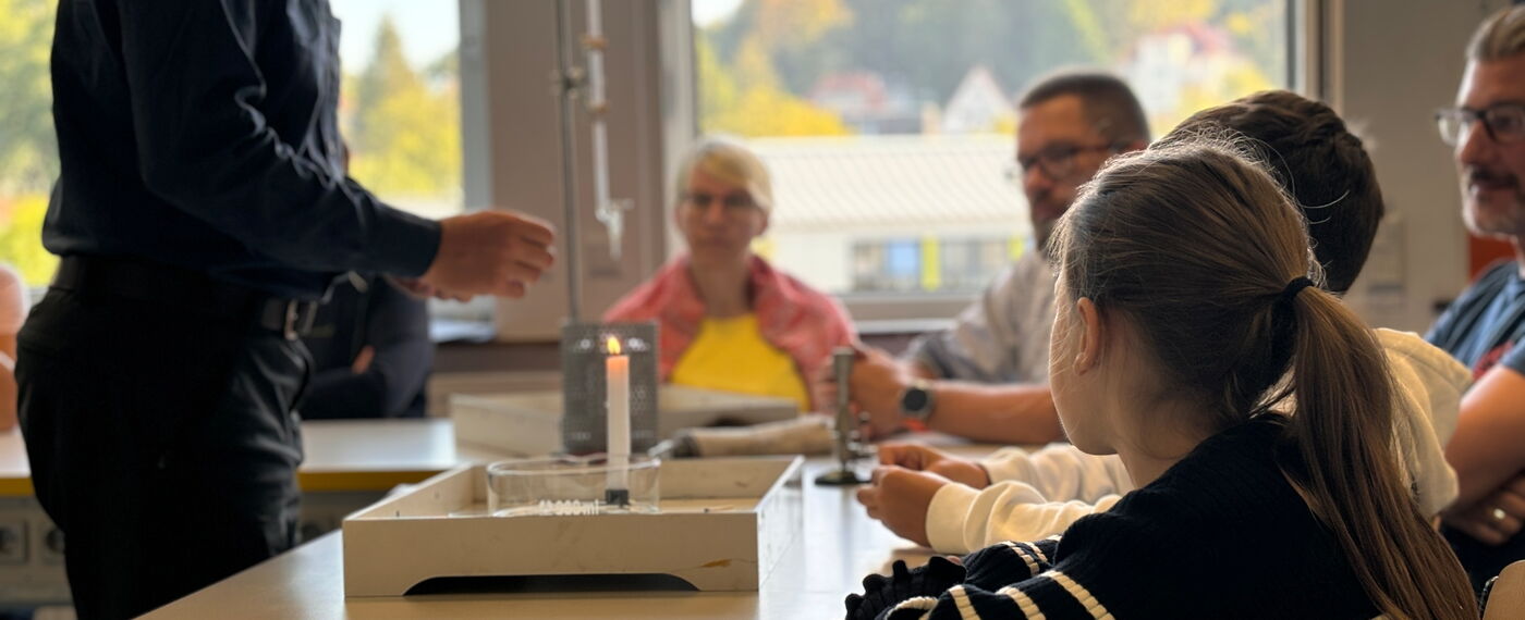 ein Lehrer demonstriert eine Experiment mit einer Kerze vor Schüler*innen und Lehrer*innen.