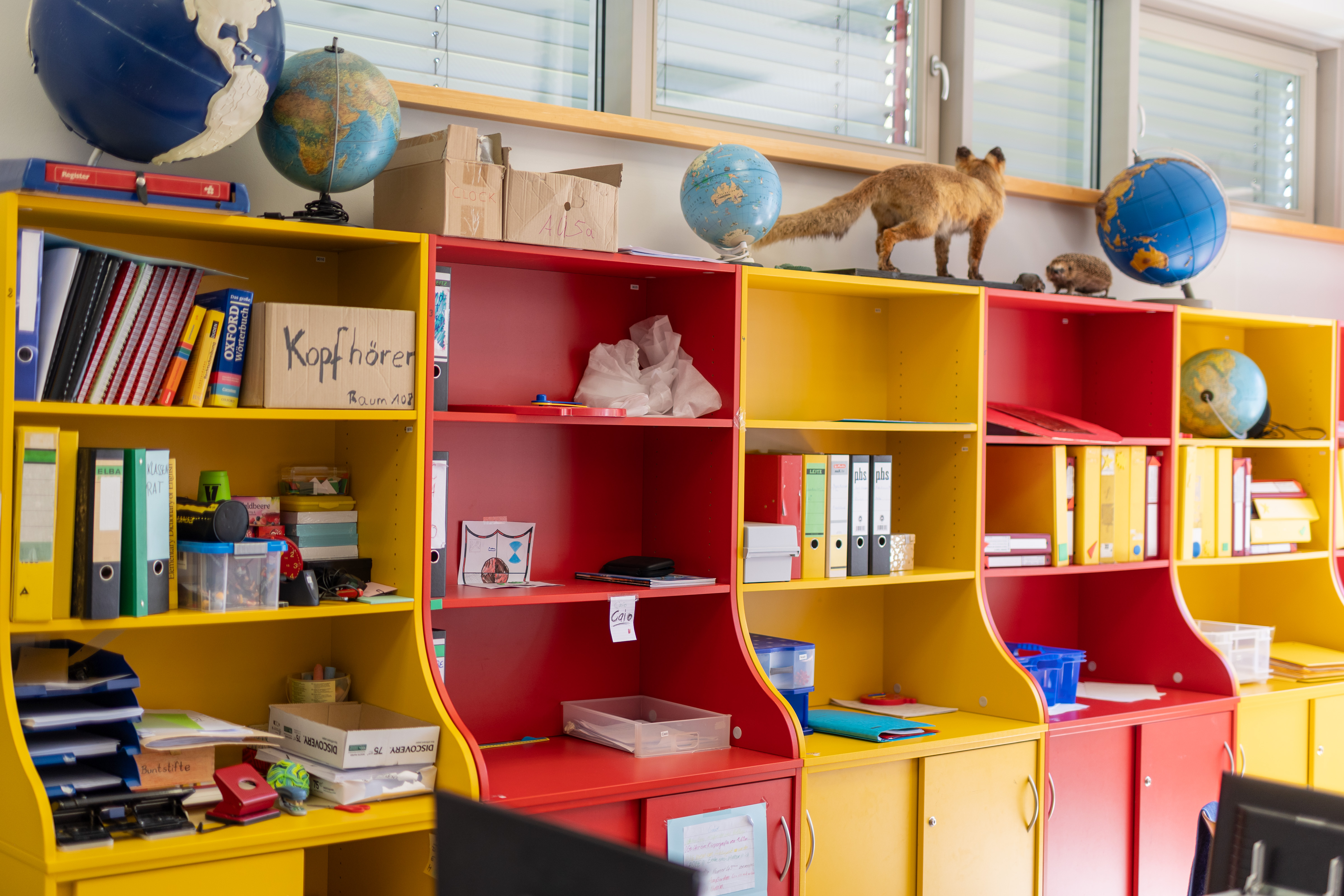 Klassenraum mit mehreren gelben und roten Regale, in denen Ordner und andere Materialien stehen.