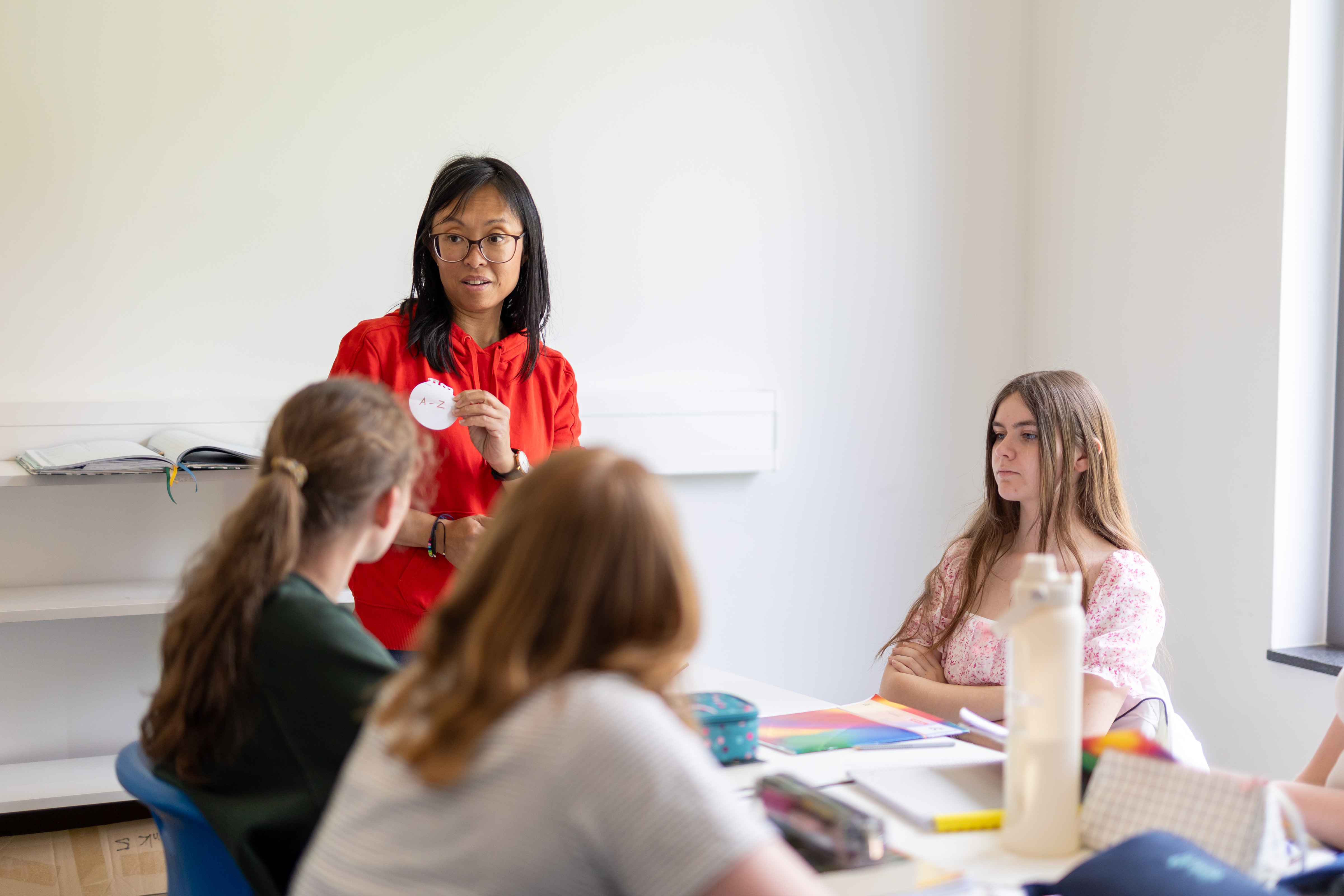 Eine Lernbegleiterin hält einen runden Zettel in der Hand, mehrere Schüler*innen schauen zu.