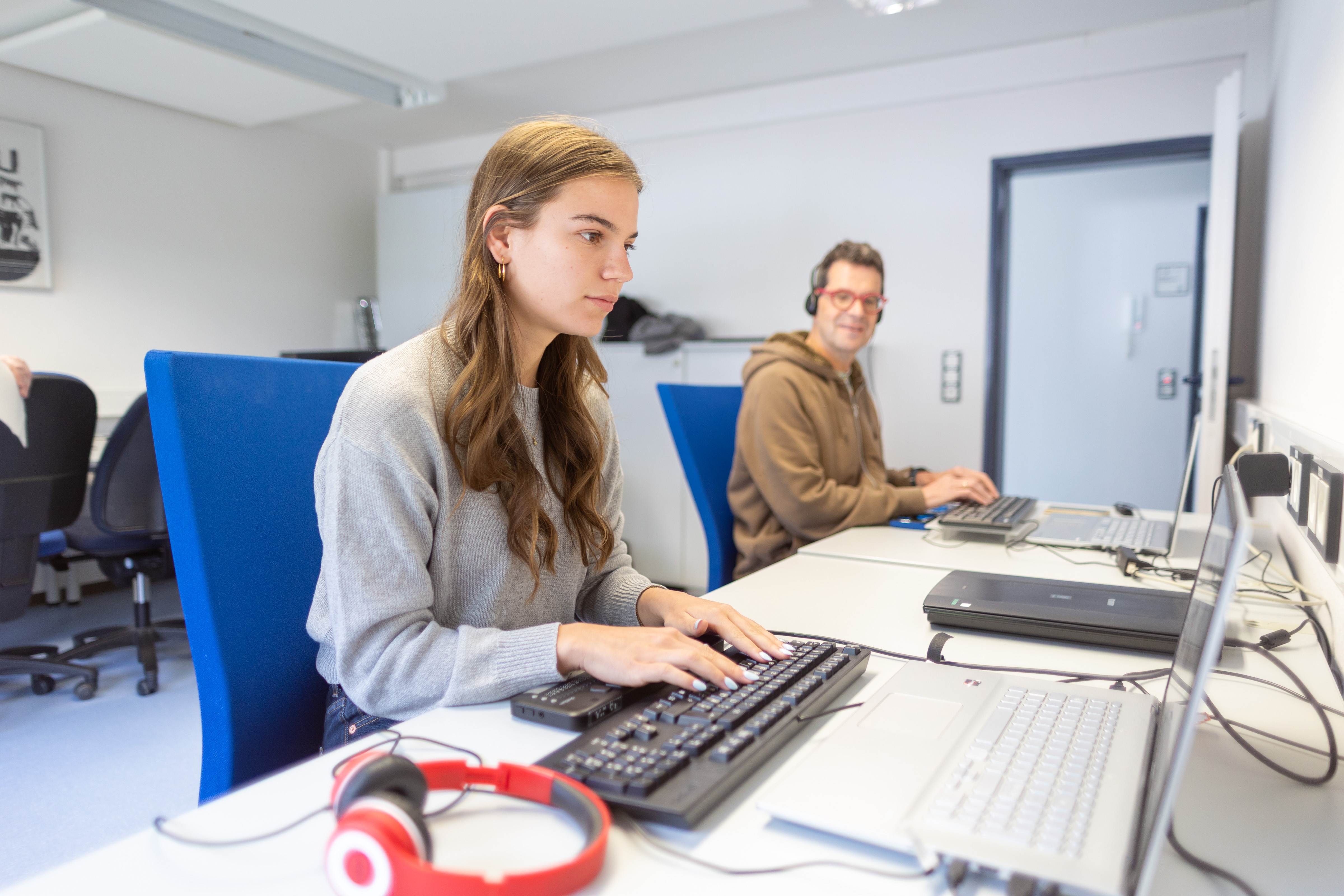 Zwei Teilnehmende sitzen in einem Unterrichtsraum und arbeiten an Laptops.
